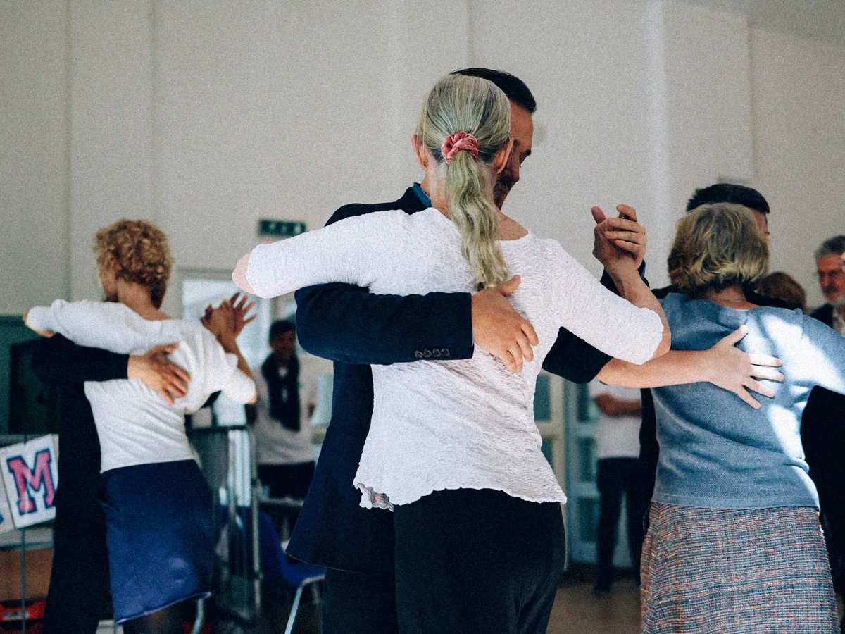 A group of adults practising a partnered dance hold in a sunlit studio (representative photograph of a couples' dance lesson, not Madero Tango's own class)