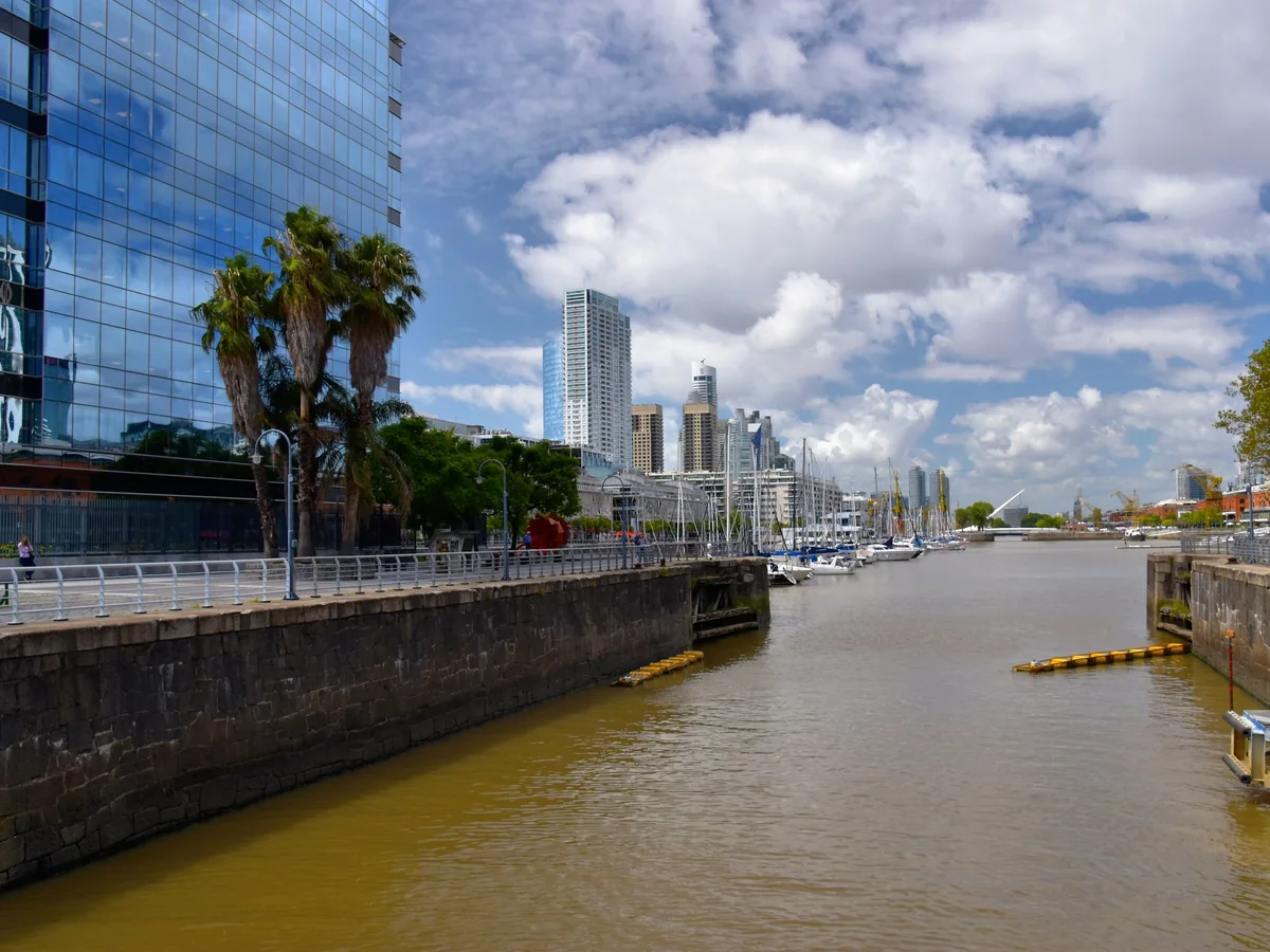 Sailboats moored along a canal in Puerto Madero, Buenos Aires, with glass office towers behind the quay